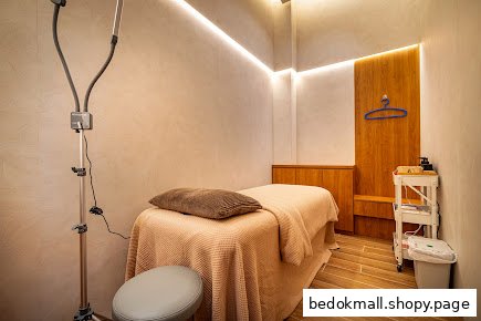 An interior treatment room with a bed, lamp, and supplies.