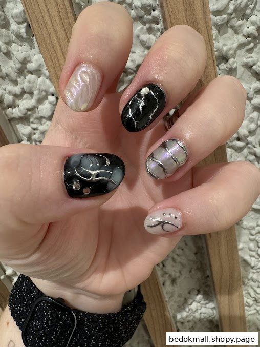 Close-up of a hand displaying black, white, and silver manicured nails.