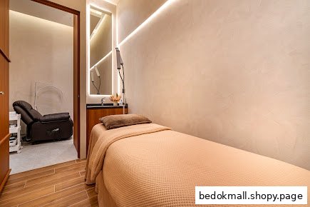 Interior room with a treatment bed, mirror, and reclining chair in background.