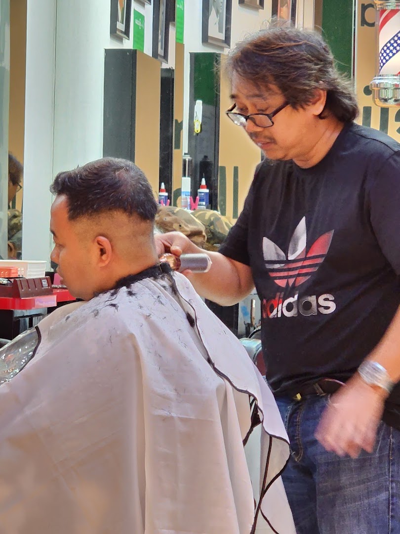A barber is cutting a customer's hair inside the shop.
