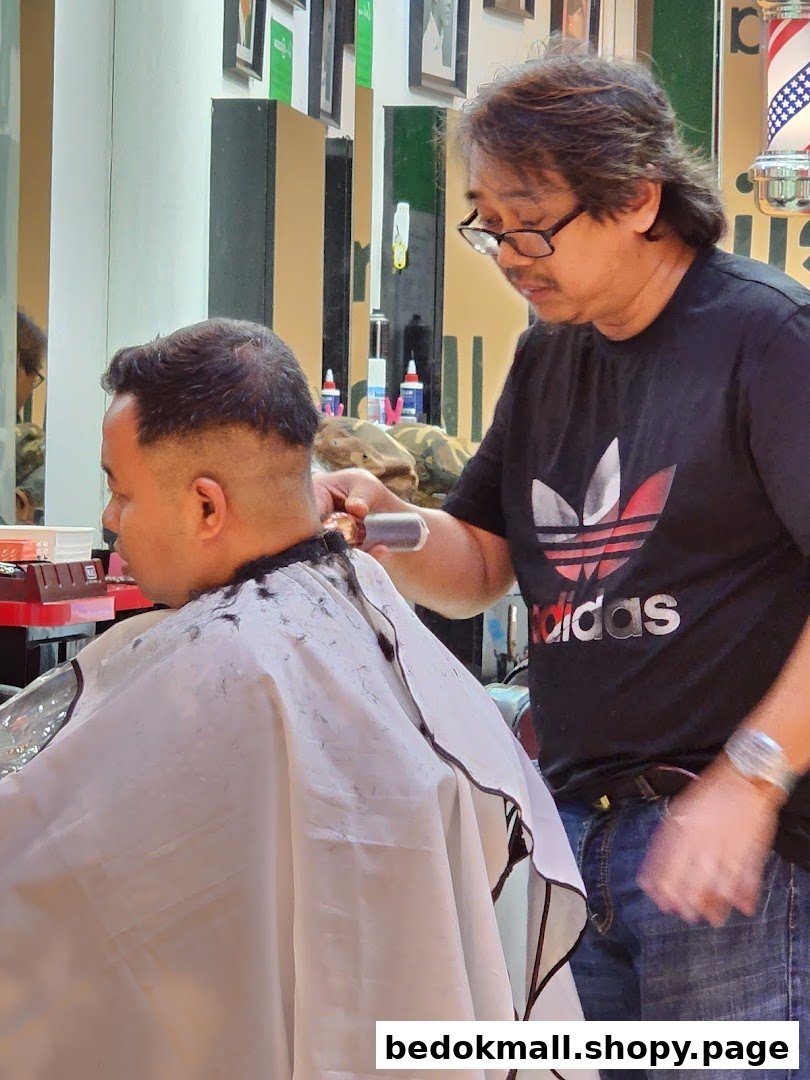 A barber is cutting a customer's hair inside the shop.
