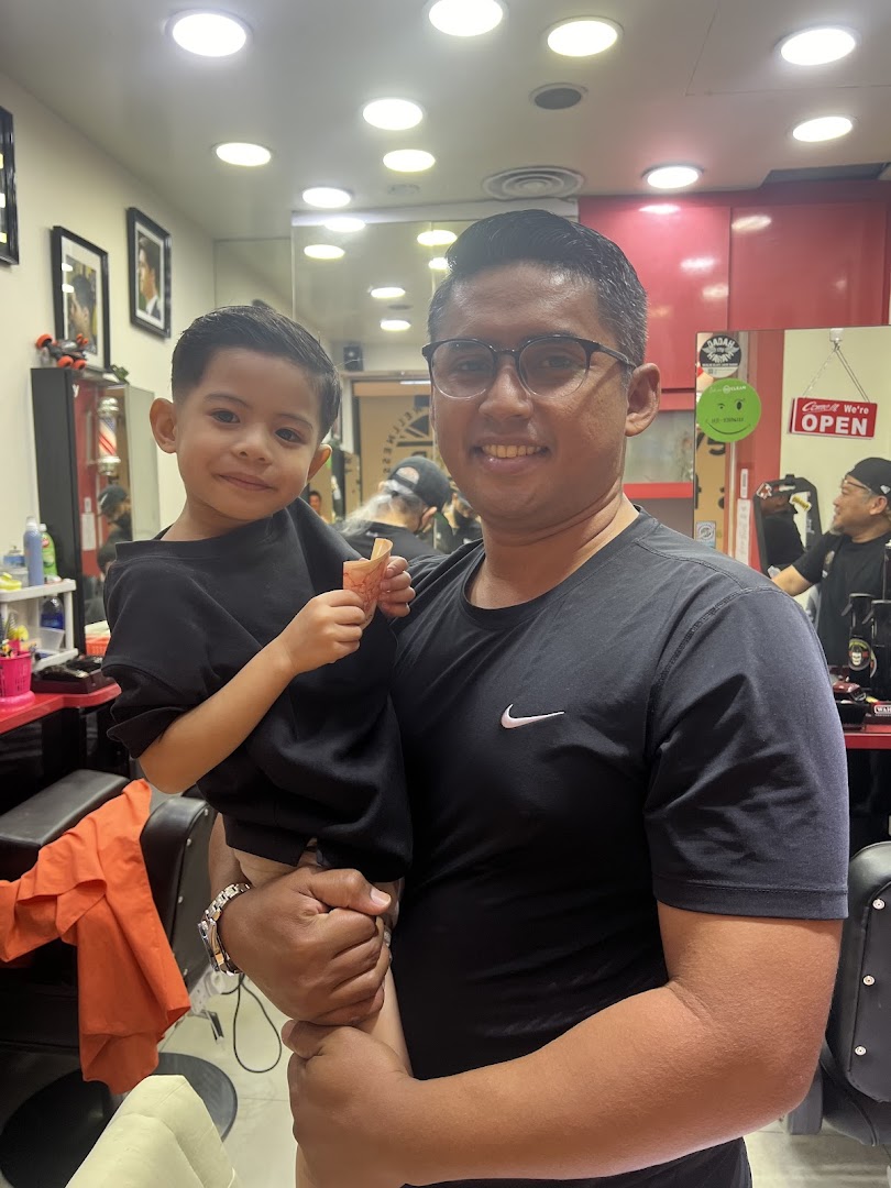 Adult and child inside a barber shop, smiling at the camera.