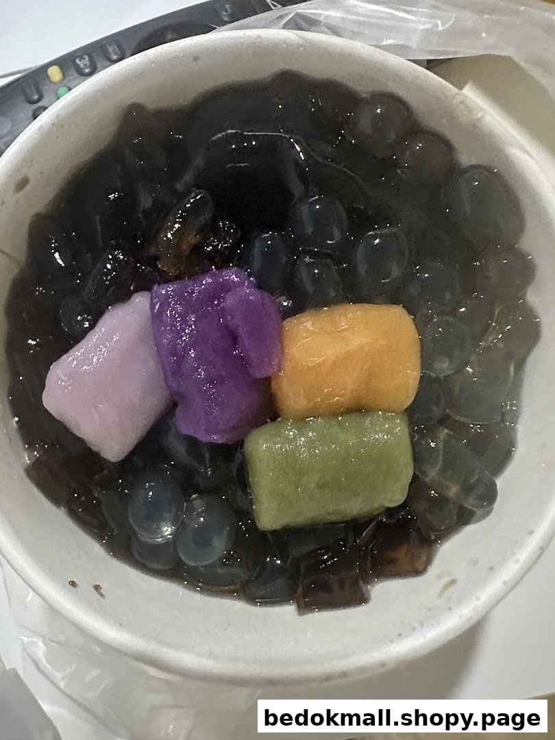 Bowl of dark dessert with colorful mochi and boba pearls.