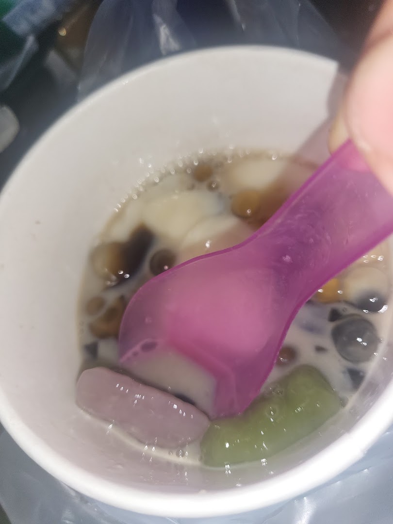 Close-up of a colorful dessert in a white cup with a purple spoon.