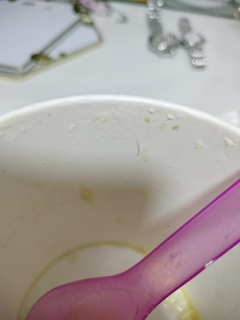 Close-up of a white cup with a purple spoon and a dark hair inside.