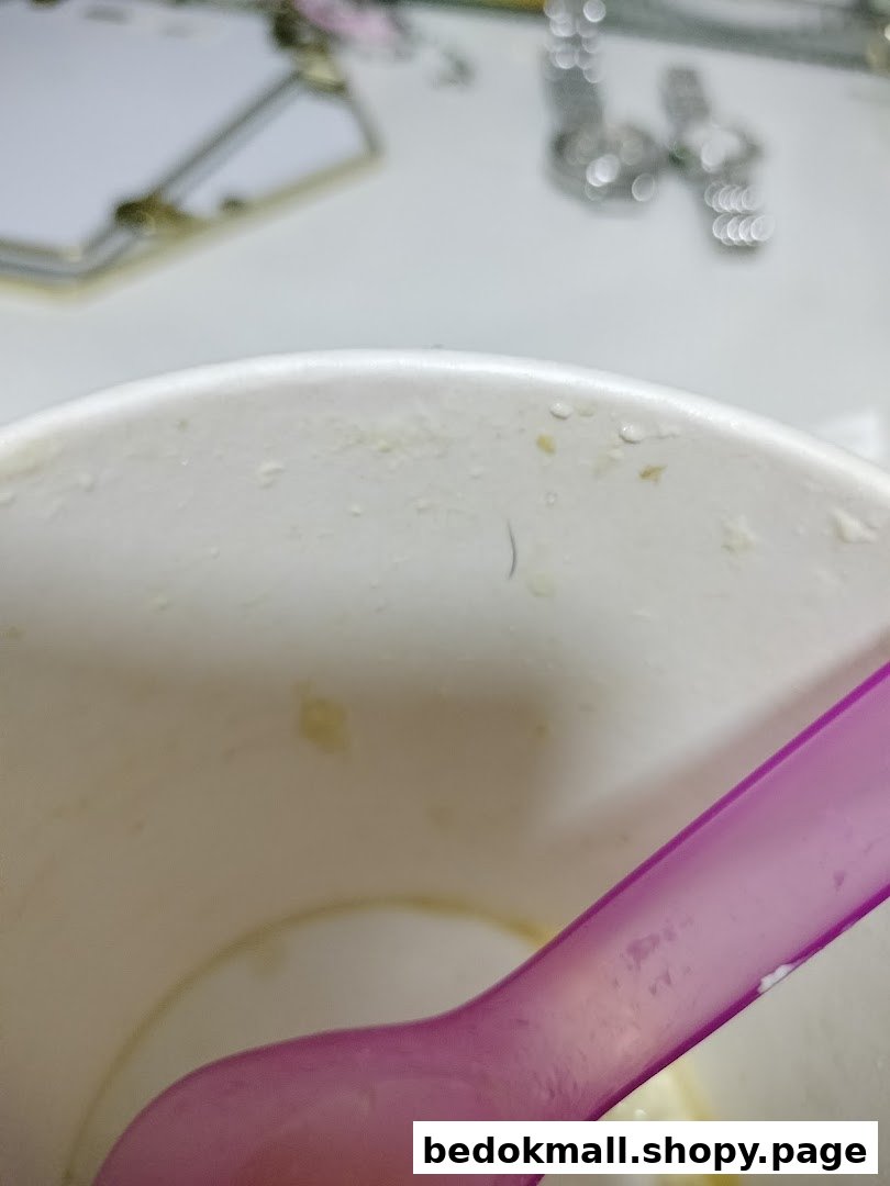 Close-up of a white cup with a purple spoon and a dark hair inside.