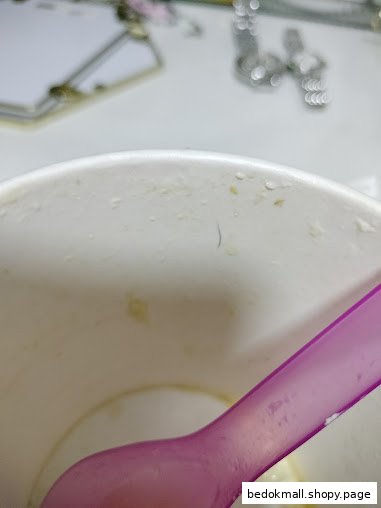 Close-up of a white dessert cup with a pink spoon and a dark strand inside.