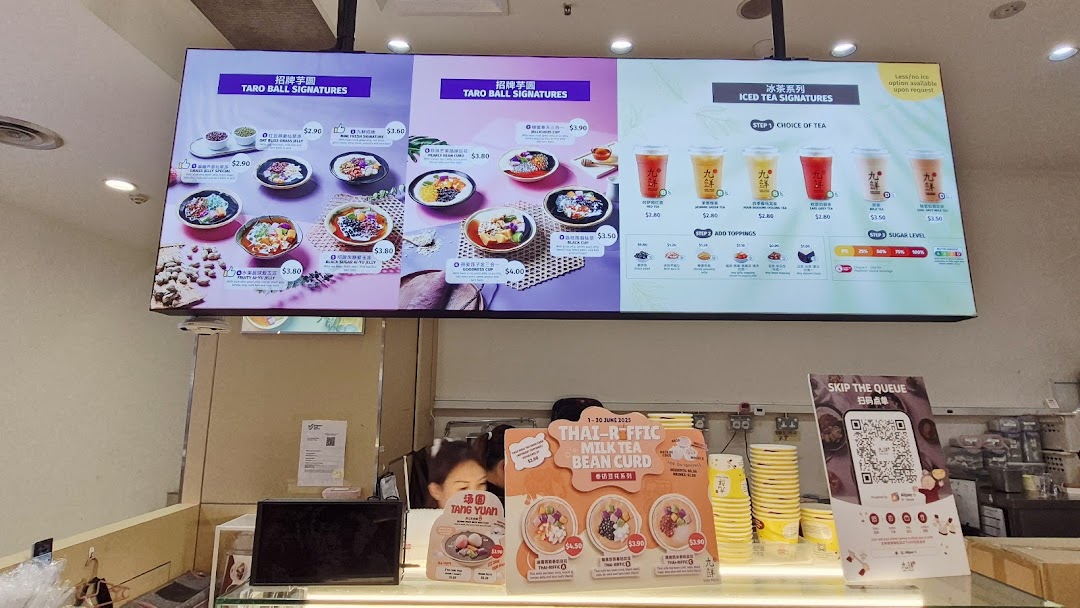 Digital menu board displaying various desserts and iced teas above a service counter.