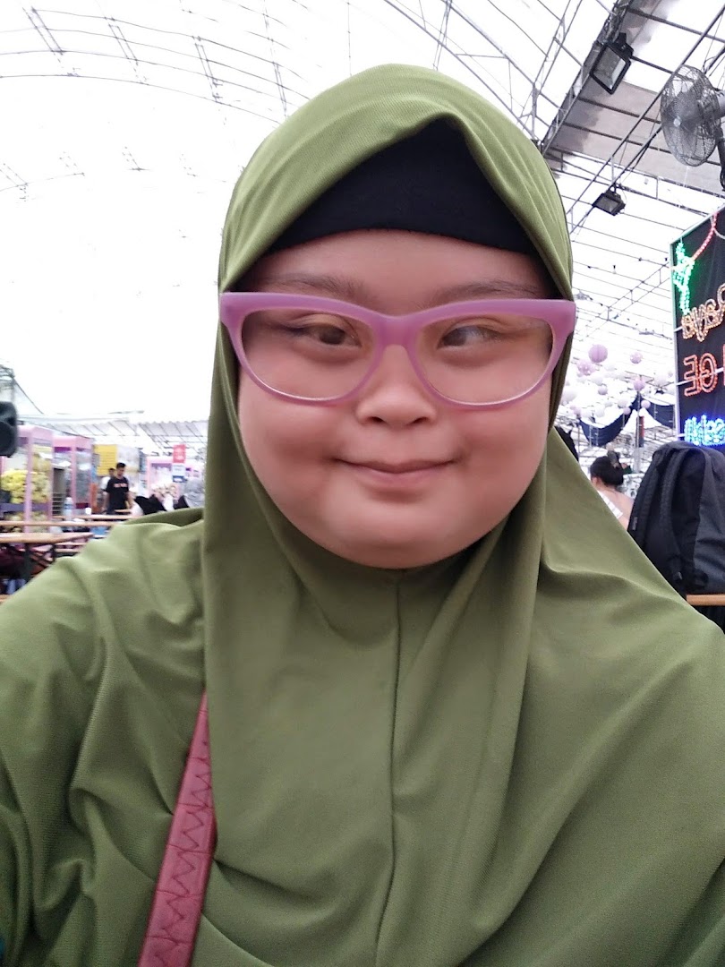 A person wearing a green hijab and pink glasses takes a selfie.