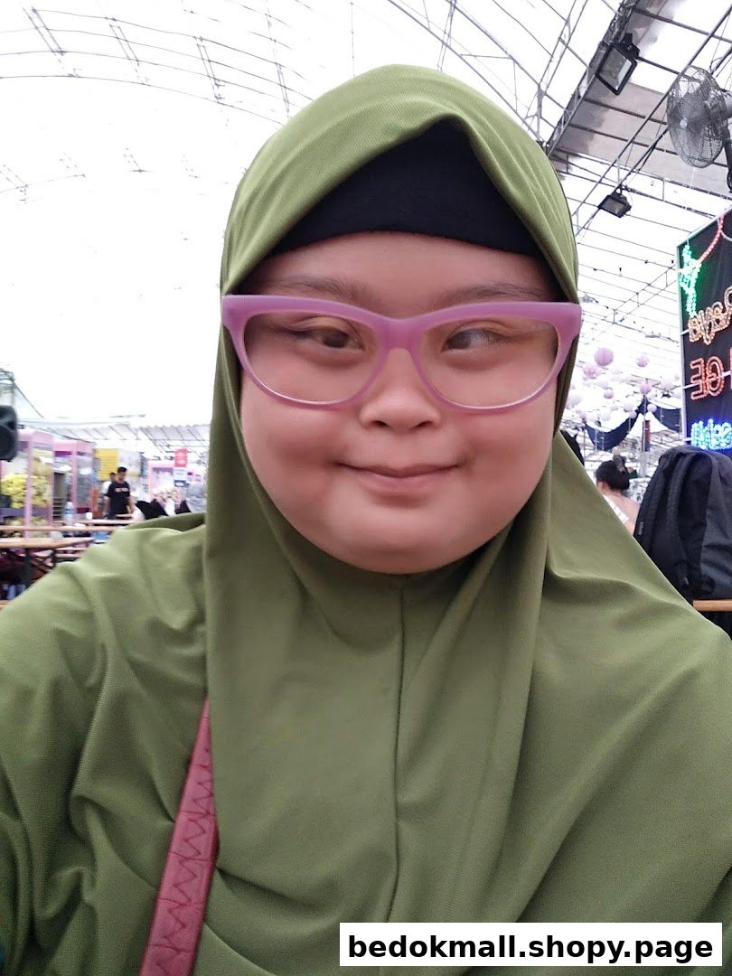 A person wearing a green hijab and pink glasses takes a selfie.
