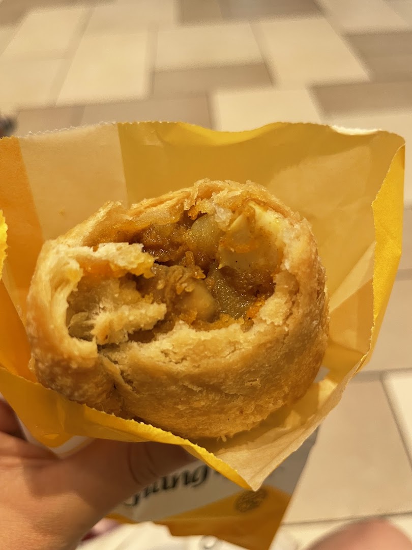 A partially eaten curry puff in a yellow wrapper.
