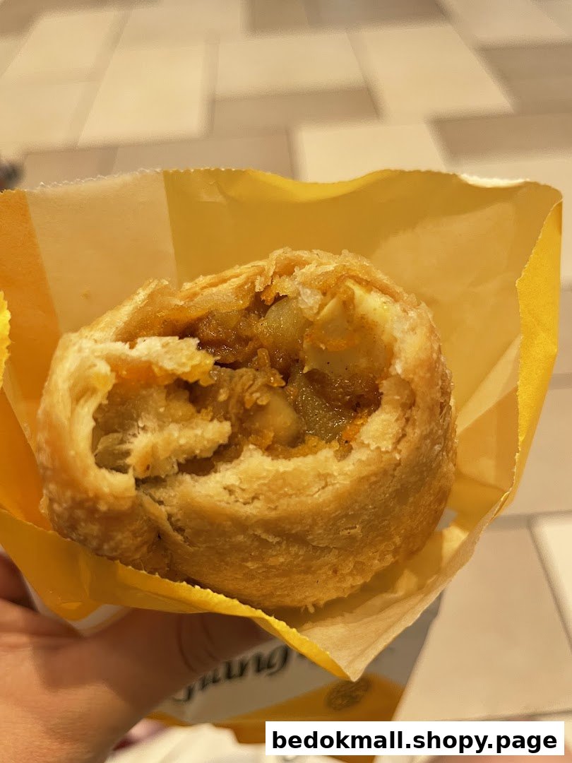 A partially eaten curry puff in a yellow wrapper.