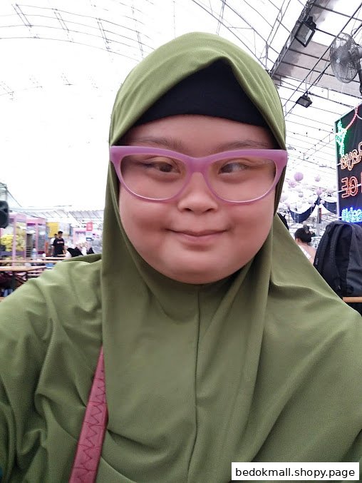 A person wearing a green hijab and pink glasses takes a selfie.