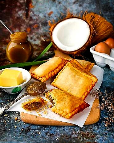 Fried pastries with coconut, eggs, and other ingredients on a wooden board.