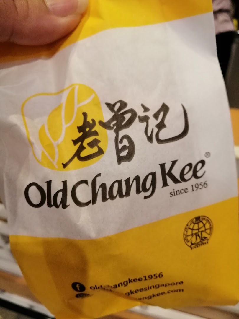 A hand holds a yellow and white Old Chang Kee branded paper bag.