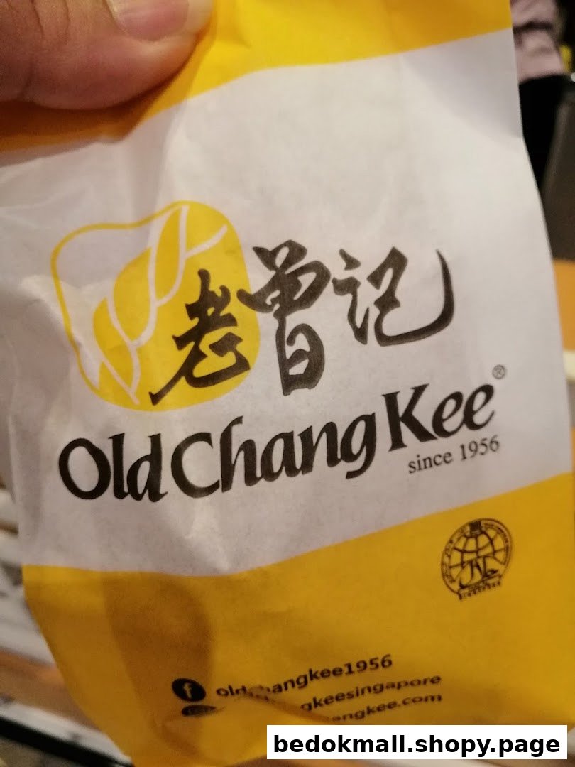 A hand holds a yellow and white Old Chang Kee branded paper bag.