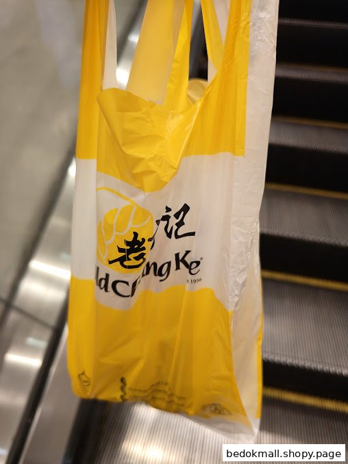 A yellow and white Old Chang Kee shopping bag hangs near an escalator.