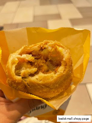 Close-up of a partially eaten curry puff in a yellow paper bag.
