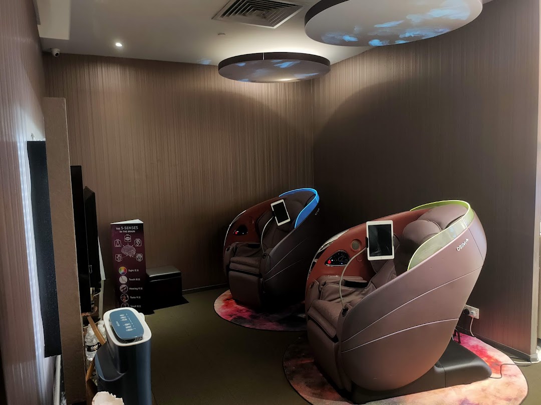 Two massage chairs are displayed in a shop interior with promotional materials.