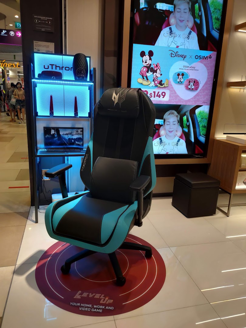Interior shop display featuring a gaming chair, product shelf, and large digital screen.