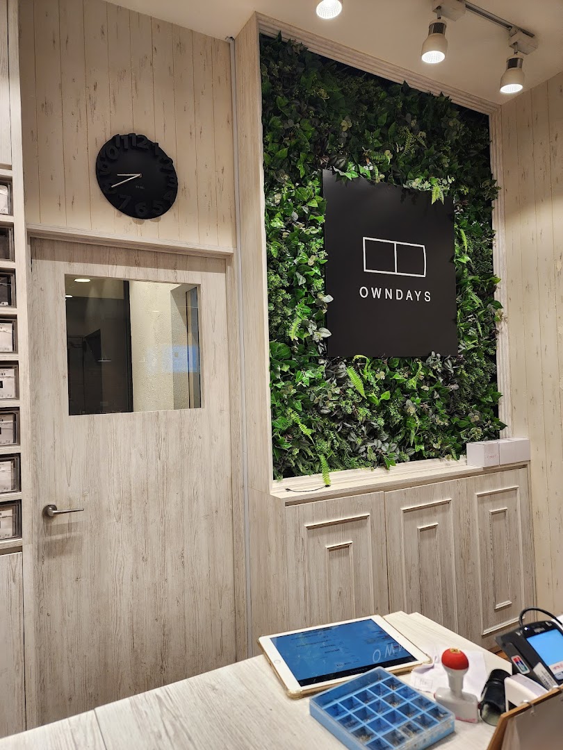 Interior view of OWNDAYS shop with counter, plant wall, and logo.