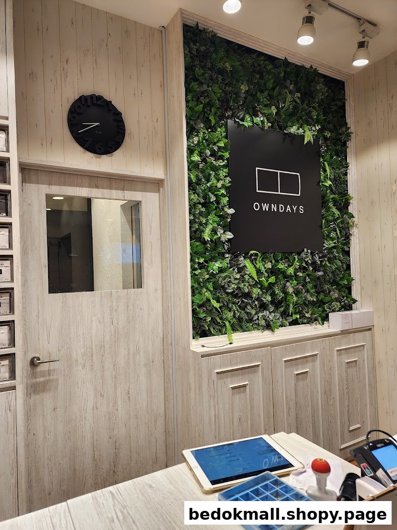 Interior view of OWNDAYS shop with counter, plant wall, and logo.