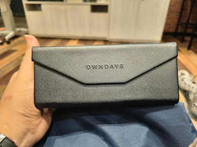Hand holding a black OWNDAYS glasses case with a blue cleaning cloth.