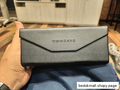Hand holding a black OWNDAYS glasses case with a blue cleaning cloth.