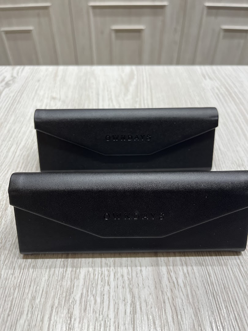 Two black OWNDAYS eyewear cases on a light wooden surface.