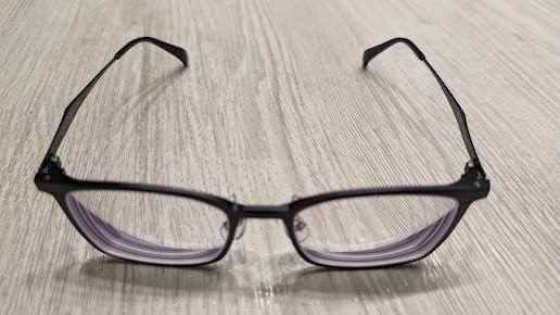 Black-framed eyeglasses resting on a light wooden surface.