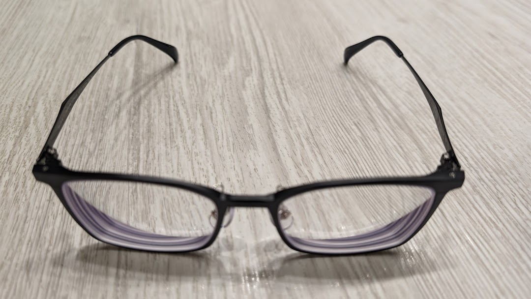 Black-framed eyeglasses with clear lenses resting on a light wooden surface.