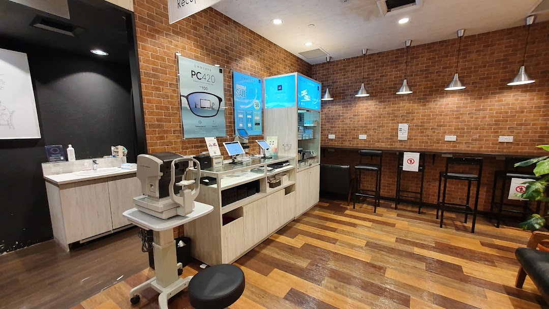 Interior of an optical shop with an eye exam machine, counter, and seating area.