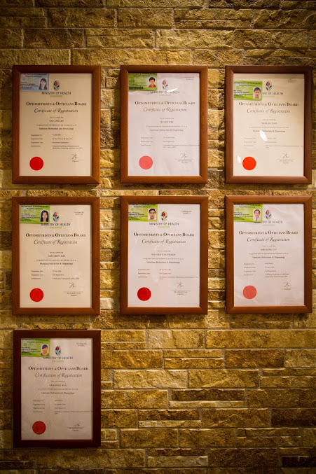 Framed optometrist registration certificates displayed on a stone wall.