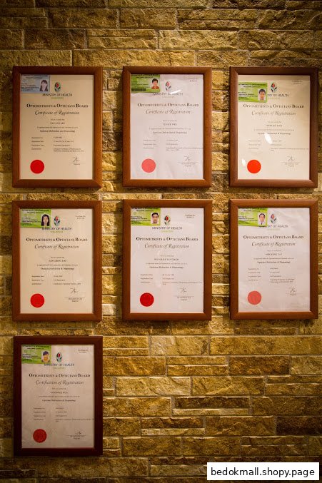 Framed optometrist registration certificates displayed on a stone wall.