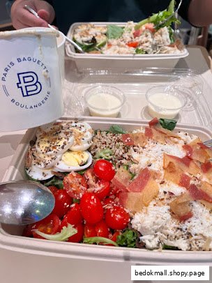 Two large salads with various toppings and a branded cup on a table.