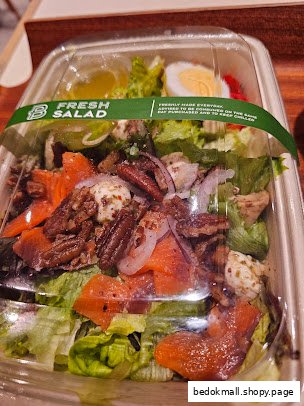 A packaged fresh salad with salmon, pecans, and egg in a clear container.