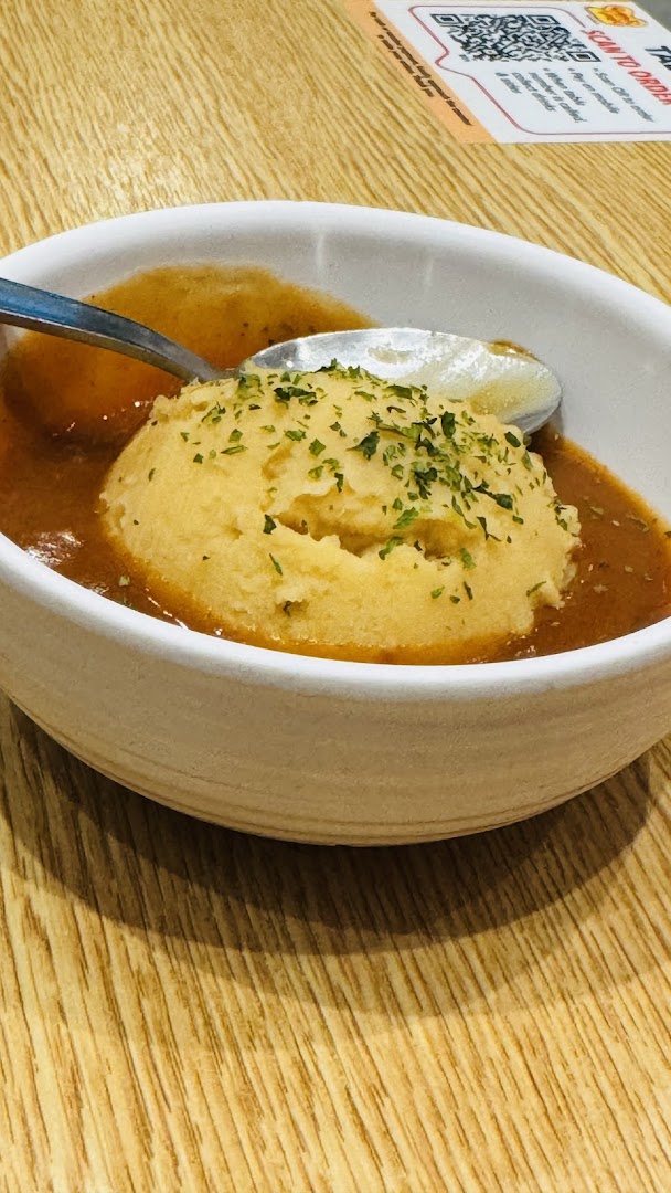 A bowl of mashed potatoes with gravy and a spoon on a wooden table.