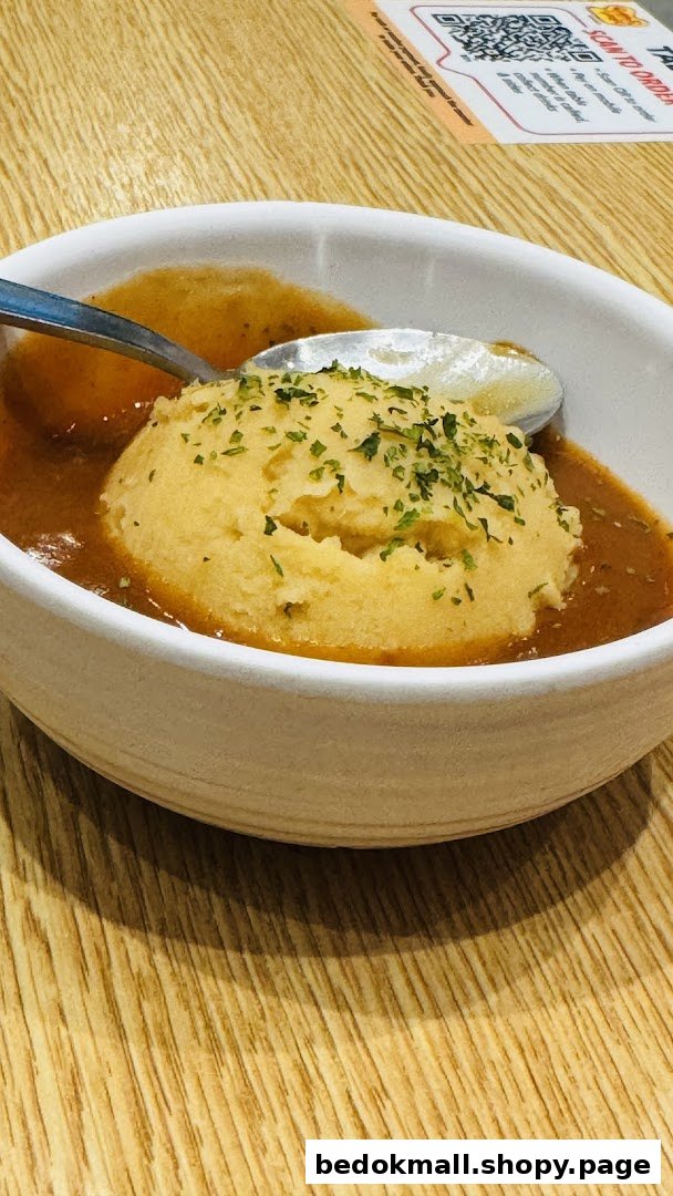 A bowl of mashed potatoes with gravy and a spoon on a wooden table.