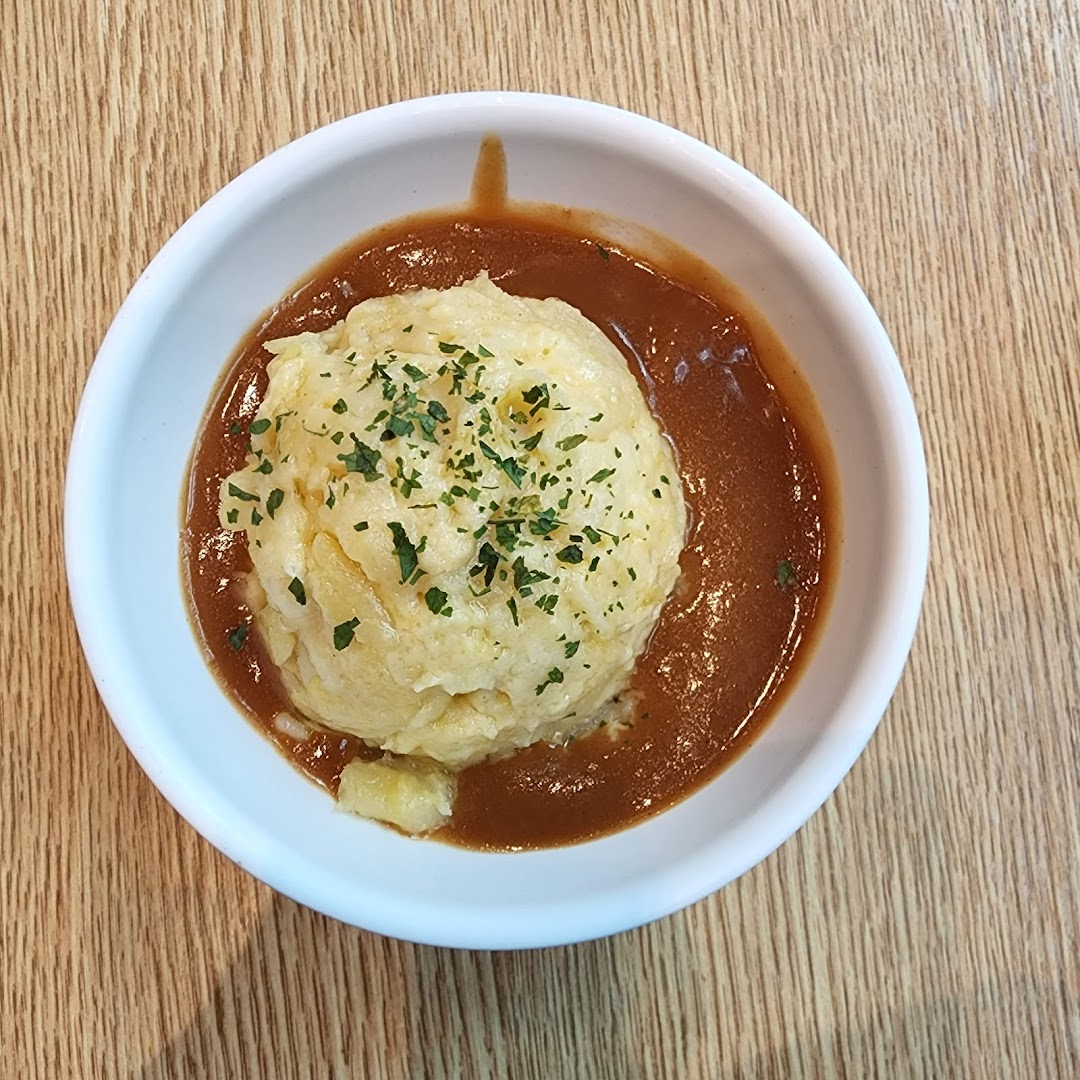 A bowl of mashed potatoes with gravy and herbs on a wooden table.