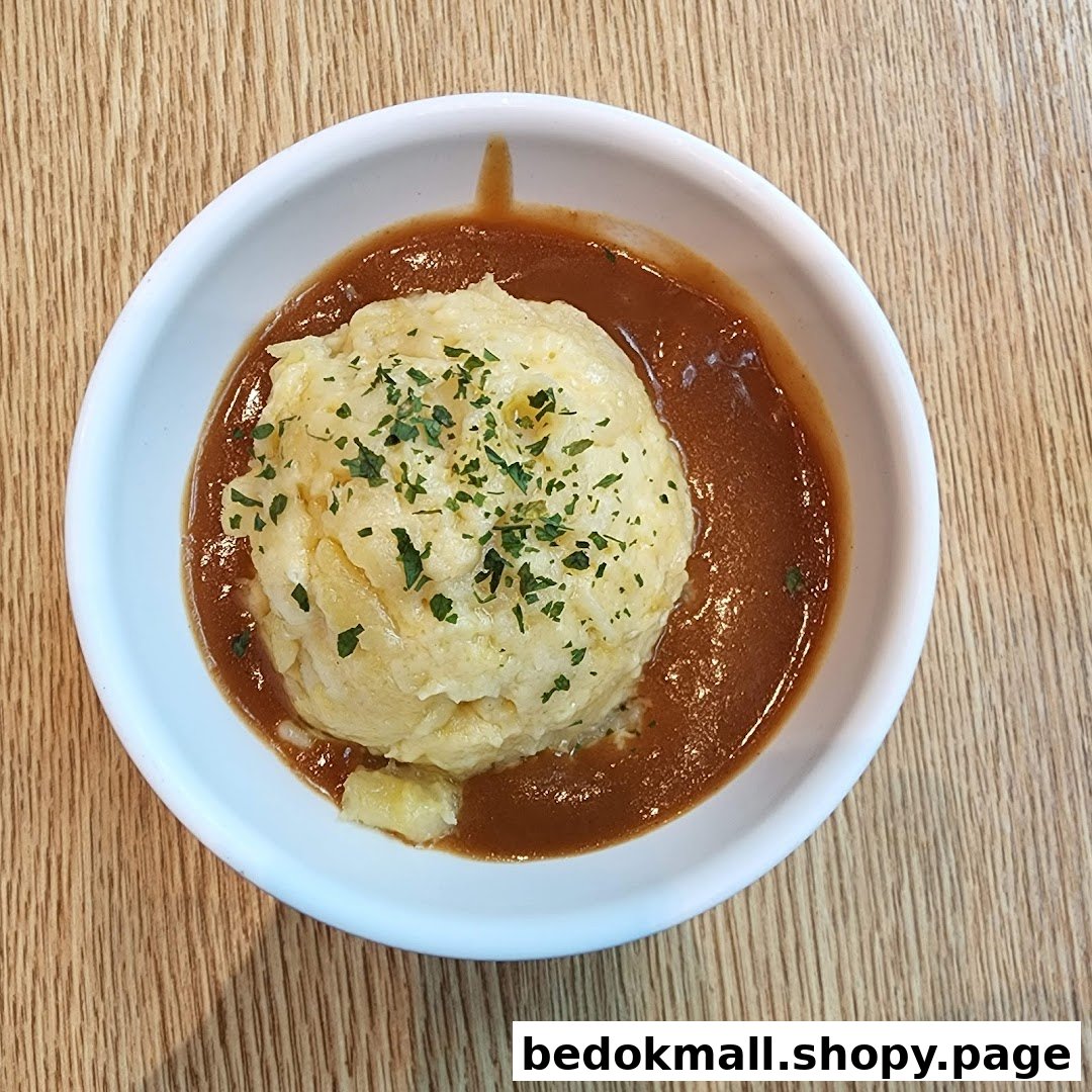 A bowl of mashed potatoes with gravy and herbs on a wooden table.