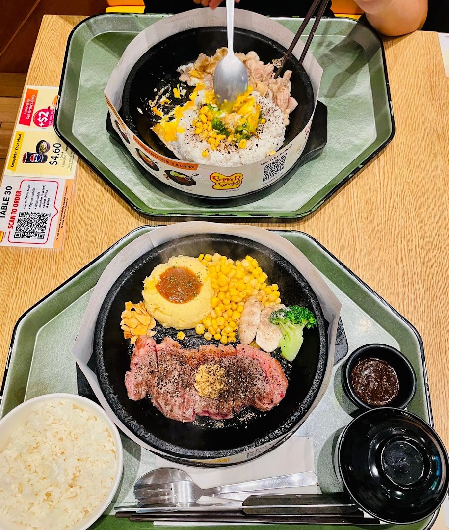 Two hot plates of food, including steak and rice dishes, on a table.