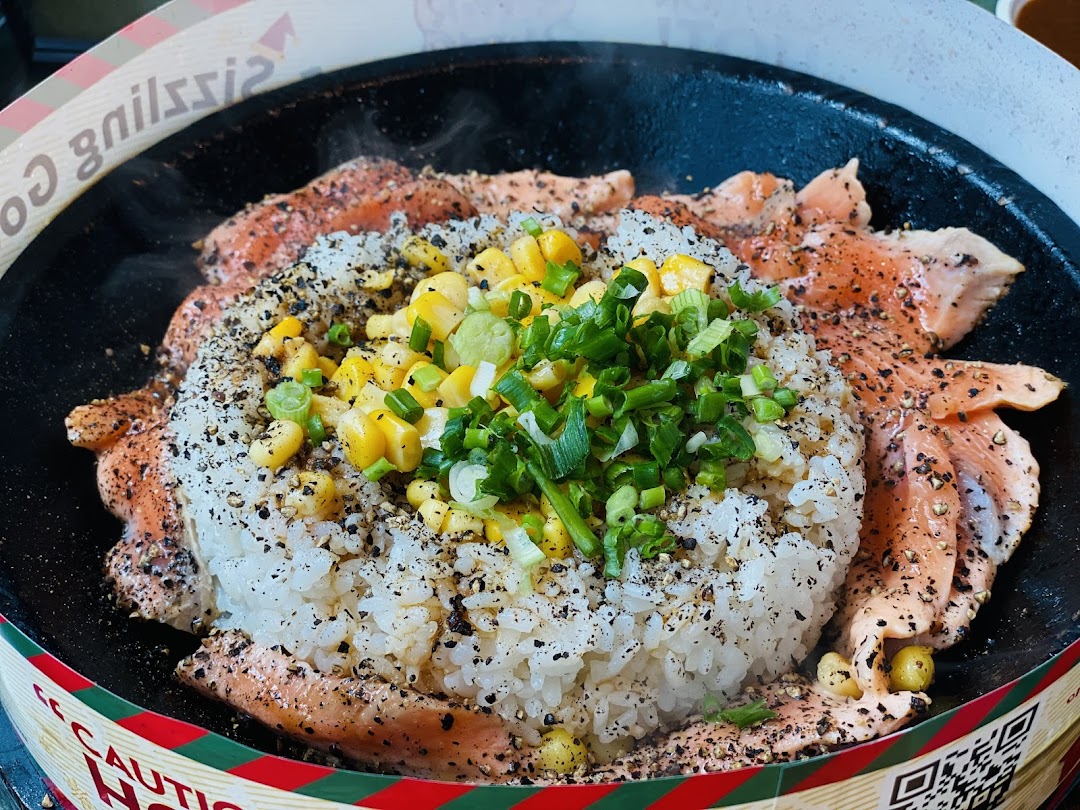 Sizzling salmon and rice dish with corn and green onions on a hot plate.