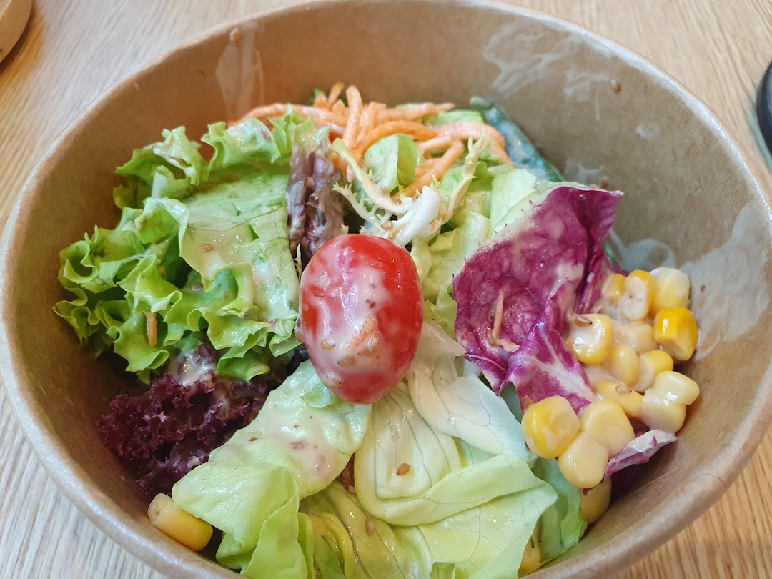 A close-up of a fresh salad with greens, tomato, and corn in a bowl.