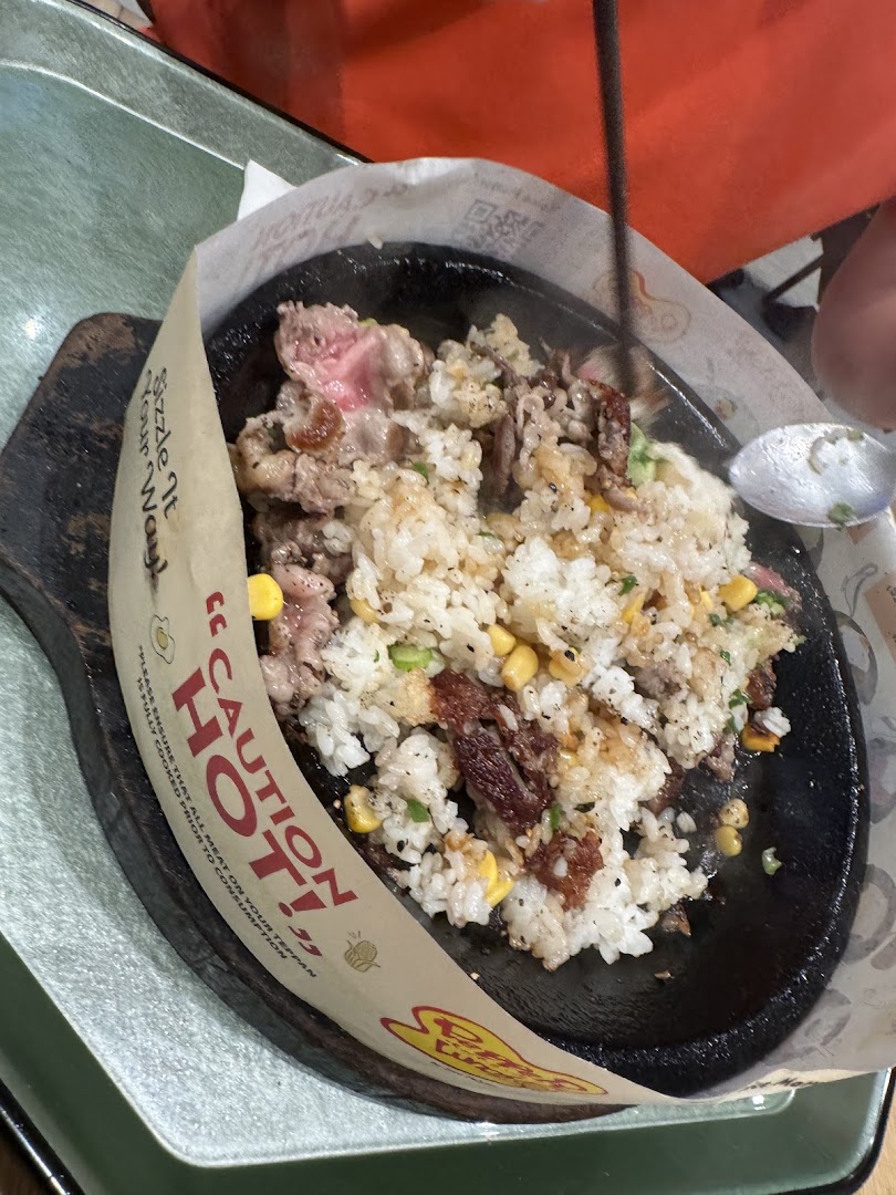 Sizzling meat and rice dish on a hot plate with chopsticks and spoon.