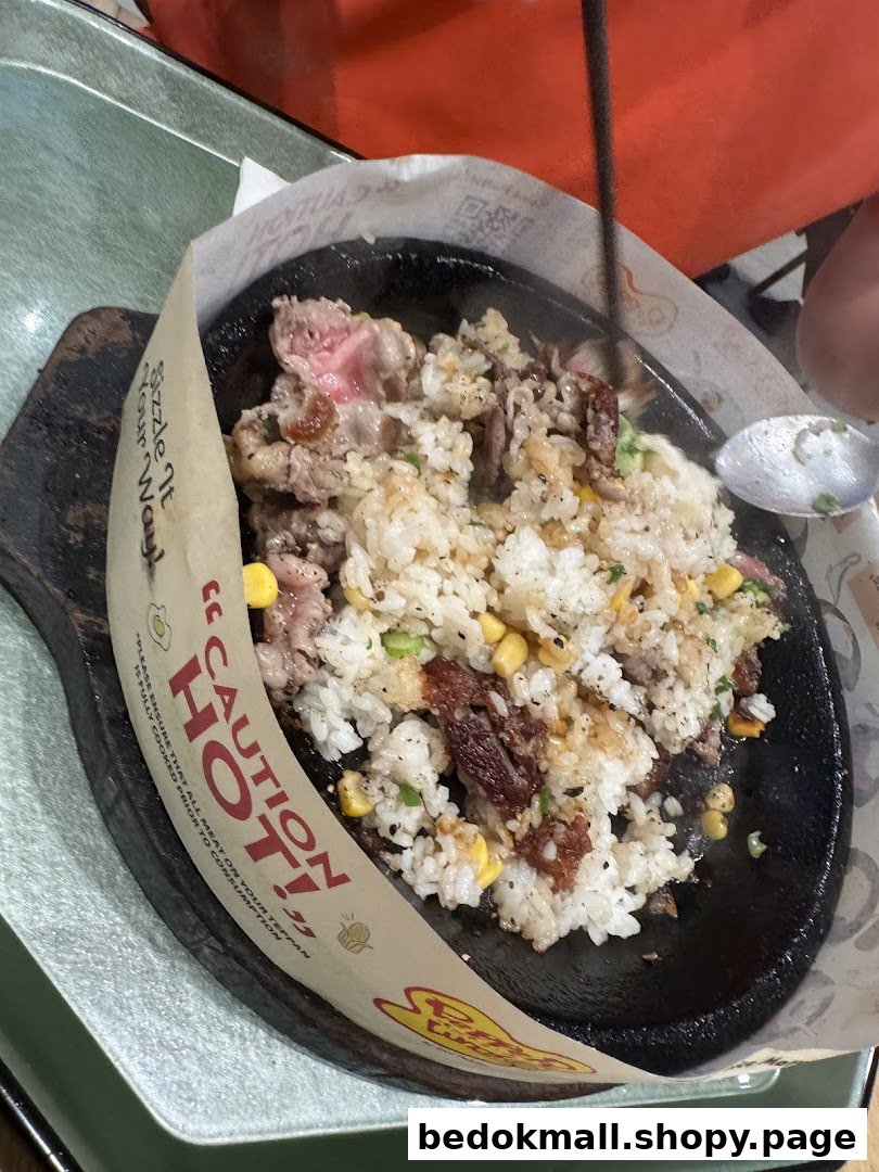 Sizzling meat and rice dish on a hot plate with chopsticks and spoon.