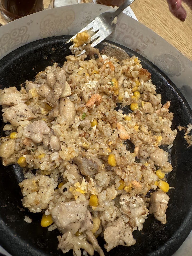 A hot plate of fried rice with chicken, corn, and salmon.