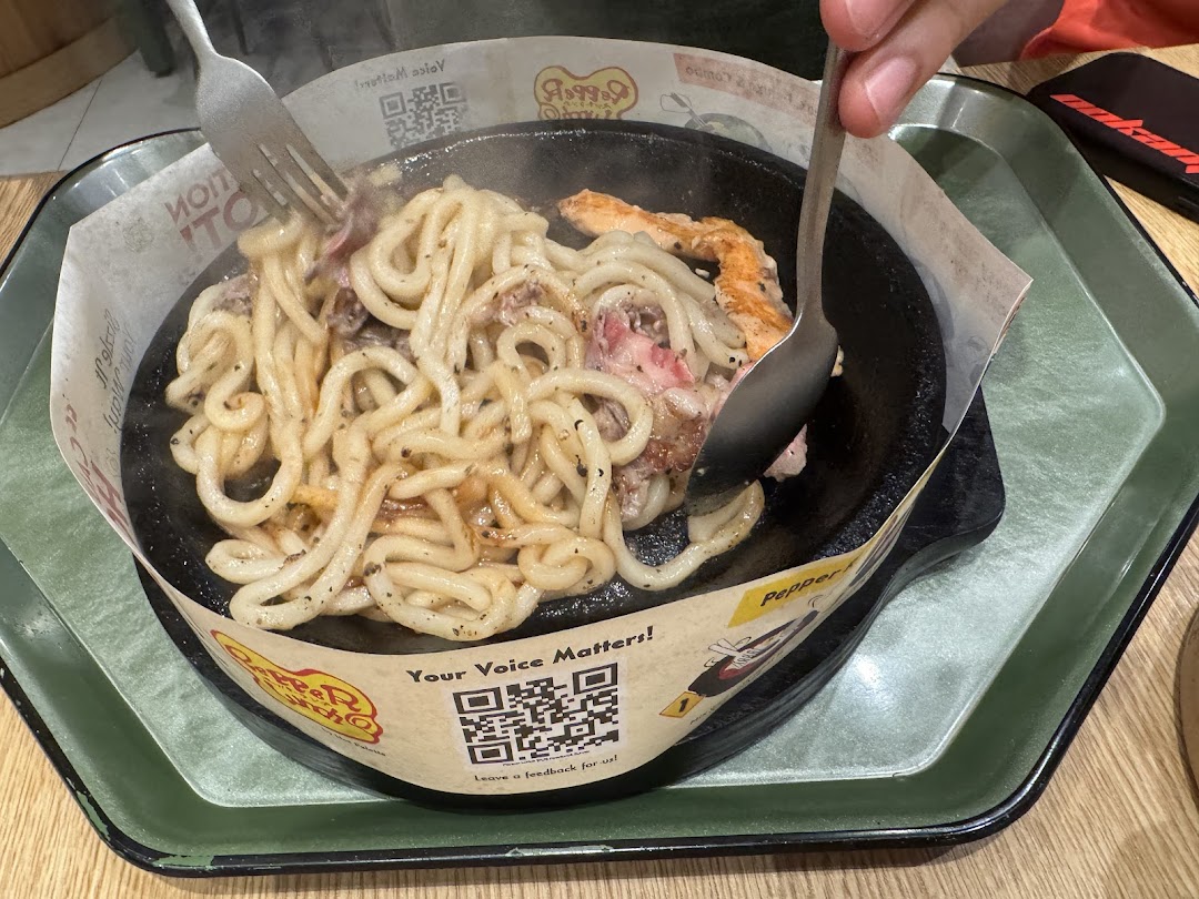Person stirring noodles and meat on a hot plate at Pepper Lunch.