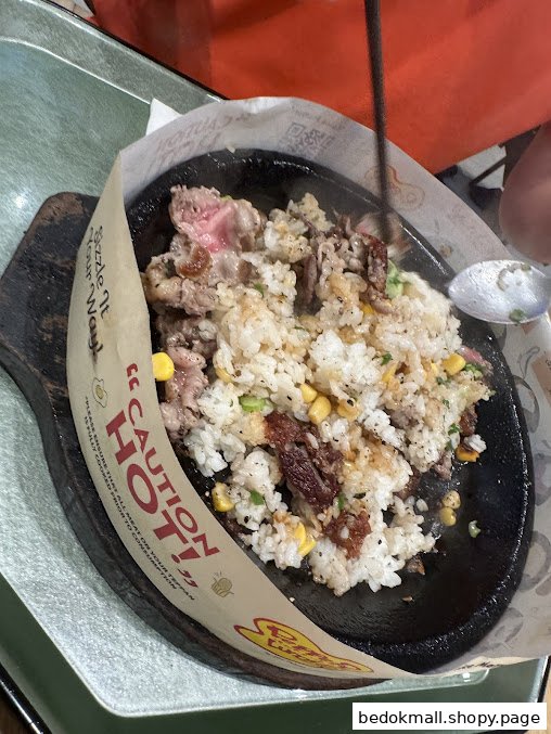 Sizzling hot plate with rice, meat, and corn being stirred.