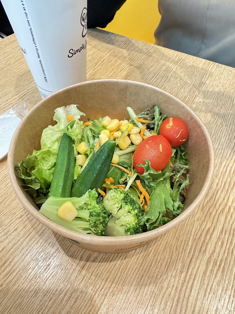 A bowl of fresh salad with various vegetables and a cup on a wooden table.