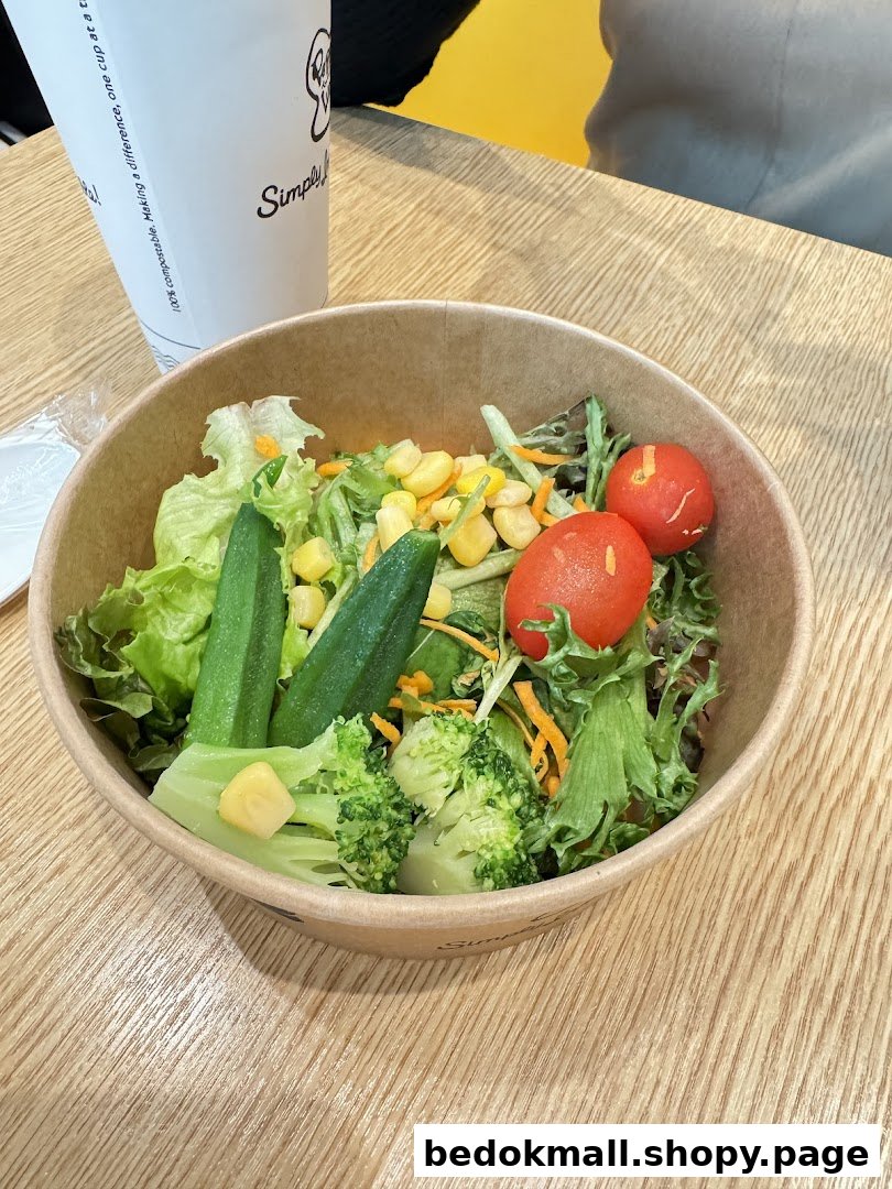 A bowl of fresh salad with various vegetables and a cup on a wooden table.